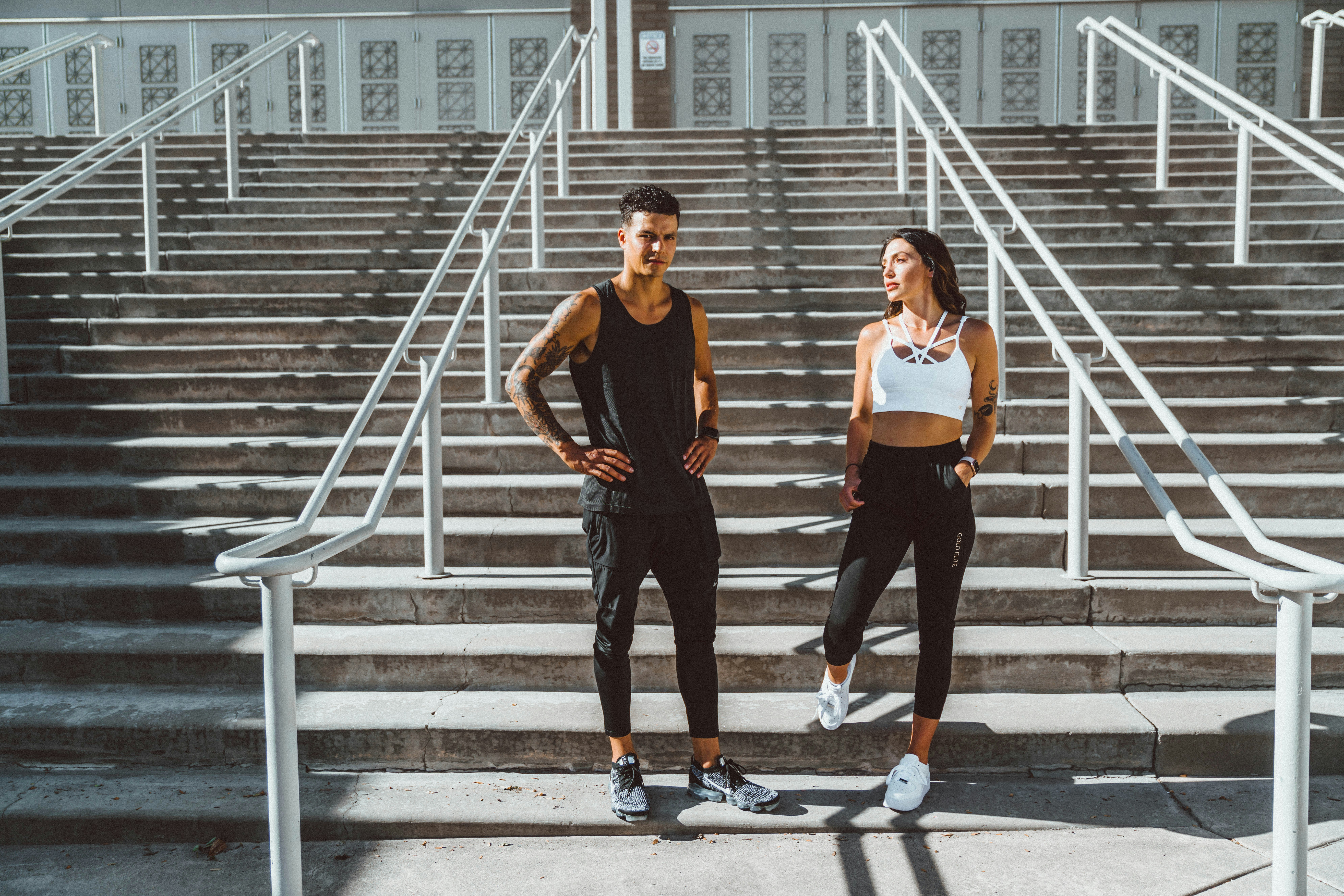 Two people in athletic wear standing on outdoor stairs in the sun.